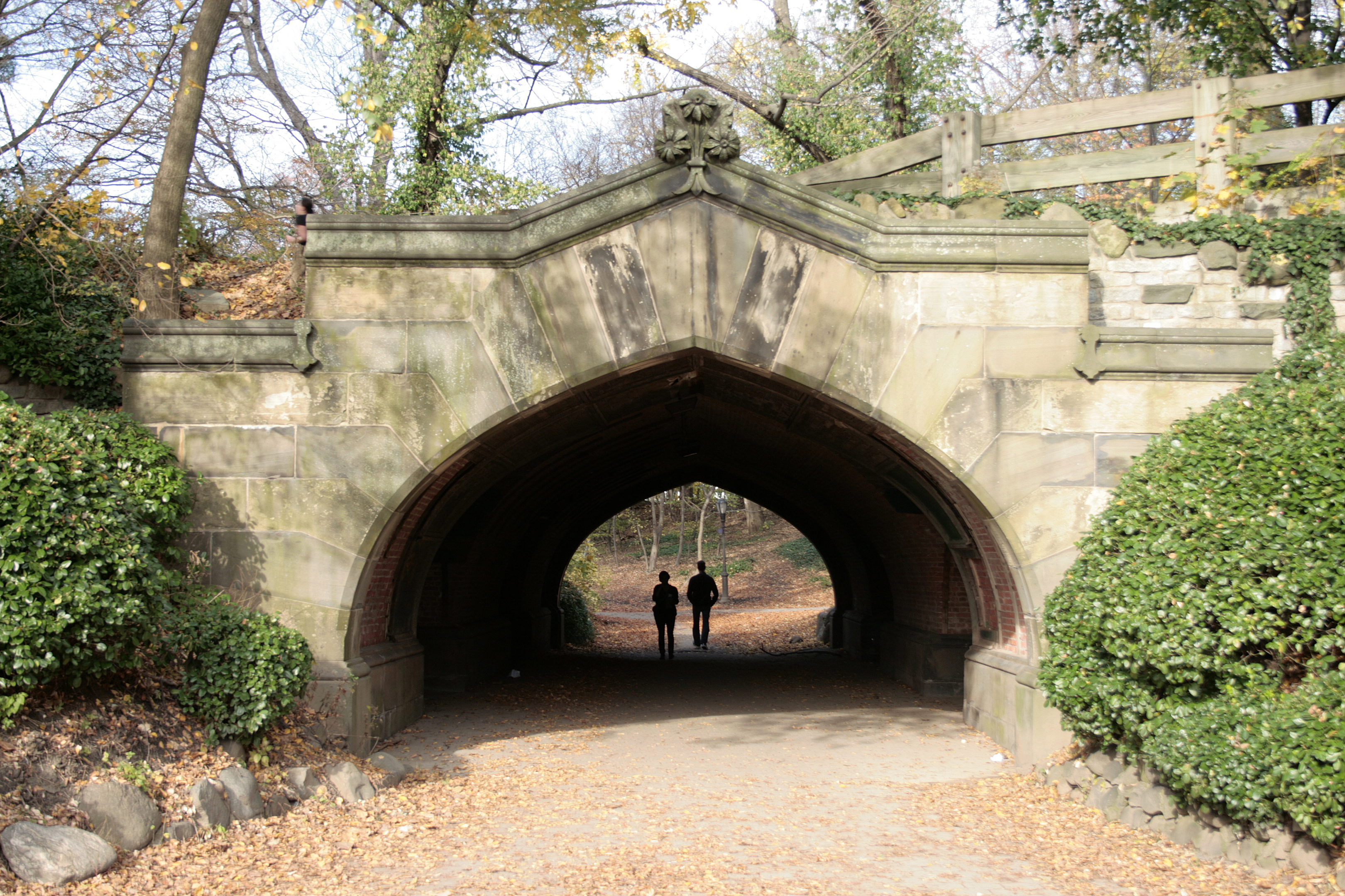 Two figures walking through a stone park bridge tunnel